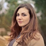 A young woman with long hair smiles confidently for an outdoor portrait session.