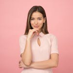 Portrait of a young woman posing elegantly in a studio with a pink background.
